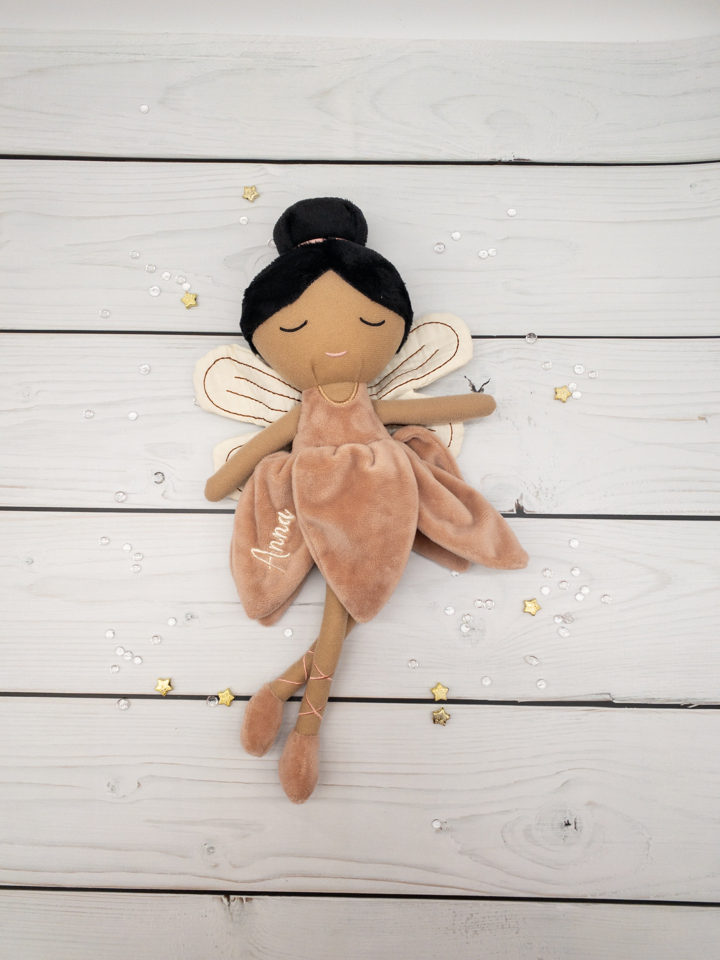Handgemachte Feenpuppe aus weichem Stoff in einem zarten Rosaton, mit Flügeln, gesticktem Namen auf dem Kleid und liebevollen Details wie Ballerinaschuhen und einer Hochsteckfrisur. Perfekt als personalisiertes Geschenk für Kinder.