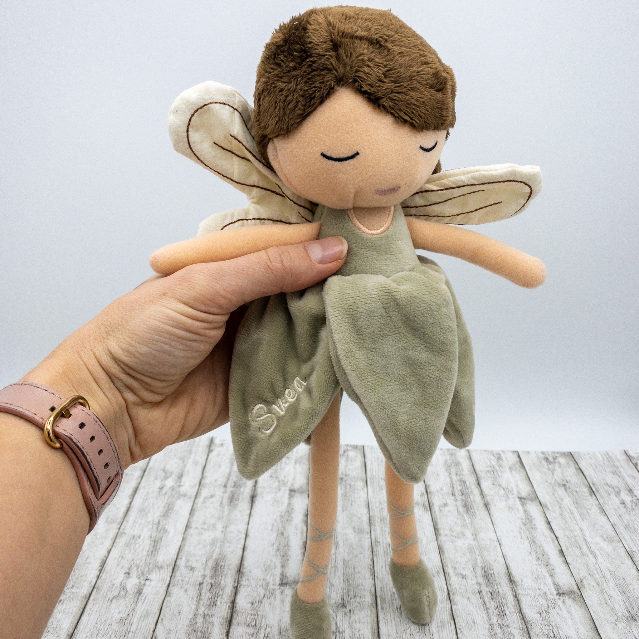 Handgefertigte Feenpuppe aus weichem Stoff in Beige, mit filigranen Flügeln, gesticktem Namen auf dem Kleid, braunen Haaren und liebevollen Details wie Ballerinaschuhen. Ideal als personalisiertes Geschenk für Kinder.
