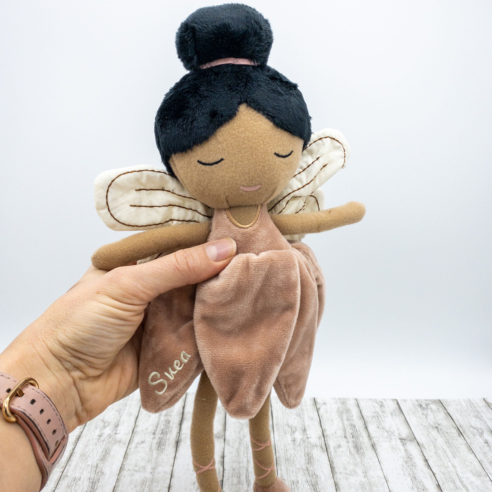 Handgemachte Feenpuppe aus weichem Stoff in einem zarten Rosaton, mit Flügeln, gesticktem Namen auf dem Kleid und liebevollen Details wie Ballerinaschuhen und einer Hochsteckfrisur. Perfekt als personalisiertes Geschenk für Kinder.