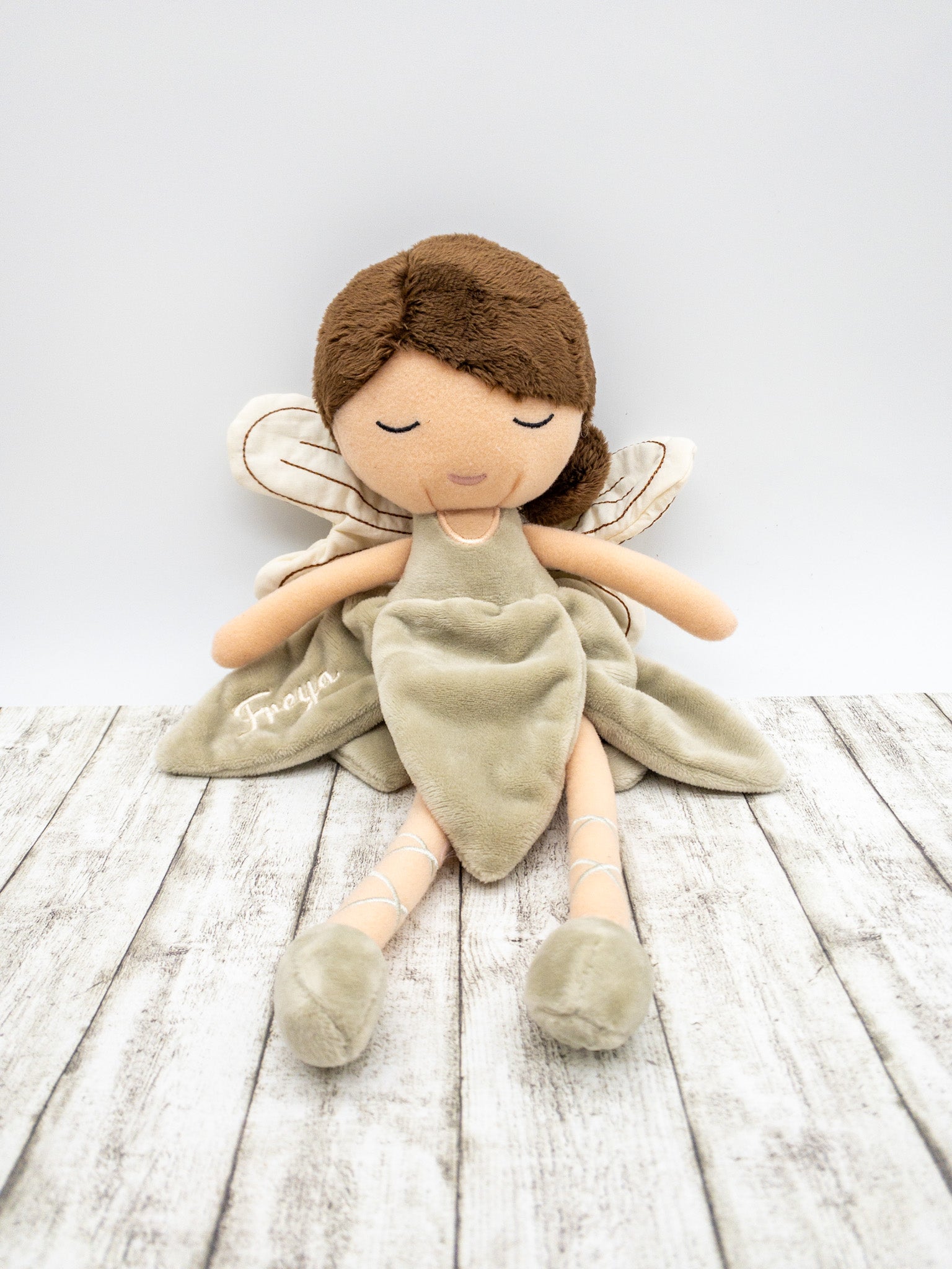 Handgefertigte Feenpuppe aus weichem Stoff in Beige, mit filigranen Flügeln, gesticktem Namen auf dem Kleid, braunen Haaren und liebevollen Details wie Ballerinaschuhen. Ideal als personalisiertes Geschenk für Kinder.