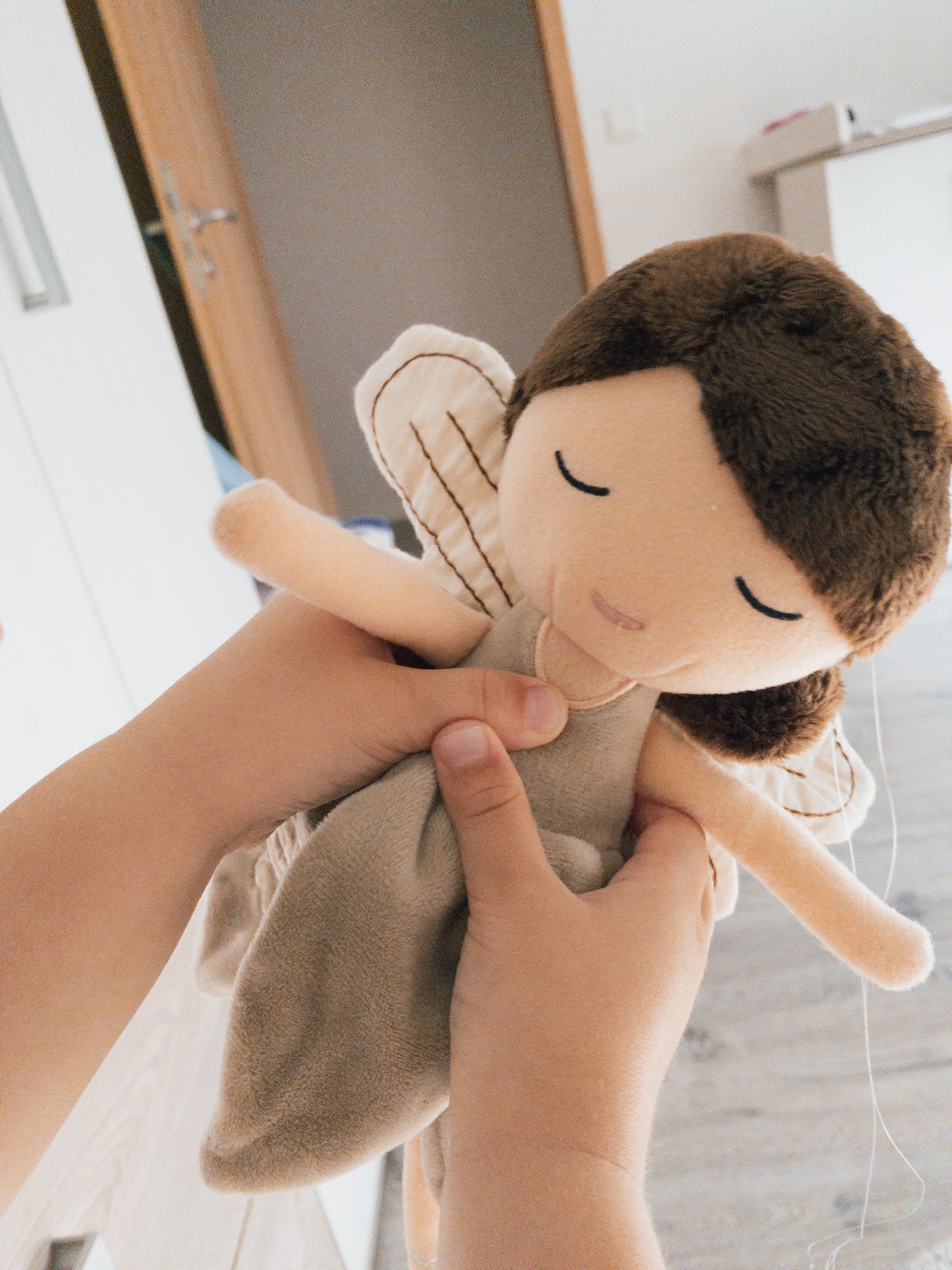 Handgefertigte Feenpuppe aus weichem Stoff in Beige, mit filigranen Flügeln, gesticktem Namen auf dem Kleid, braunen Haaren und liebevollen Details wie Ballerinaschuhen. Ideal als personalisiertes Geschenk für Kinder.