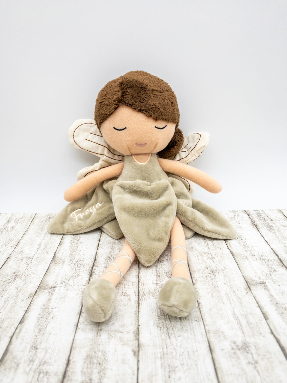 Handgefertigte Feenpuppe aus weichem Stoff in Beige, mit filigranen Flügeln, gesticktem Namen auf dem Kleid, braunen Haaren und liebevollen Details wie Ballerinaschuhen. Ideal als personalisiertes Geschenk für Kinder.